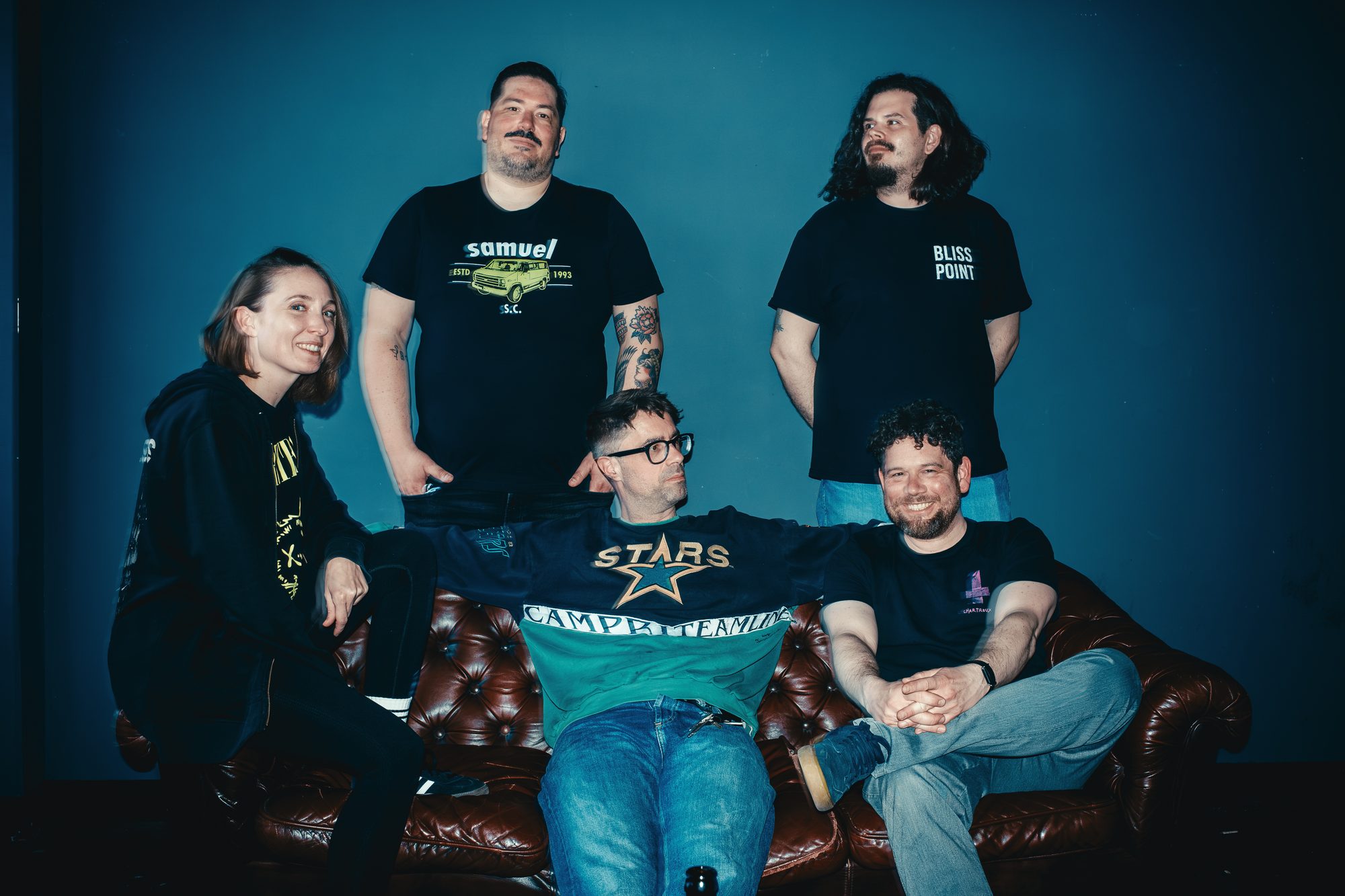 Die fünf Bandmitglieder von Bellyacher posieren gemeinsam auf einem dunklen Sofa.
