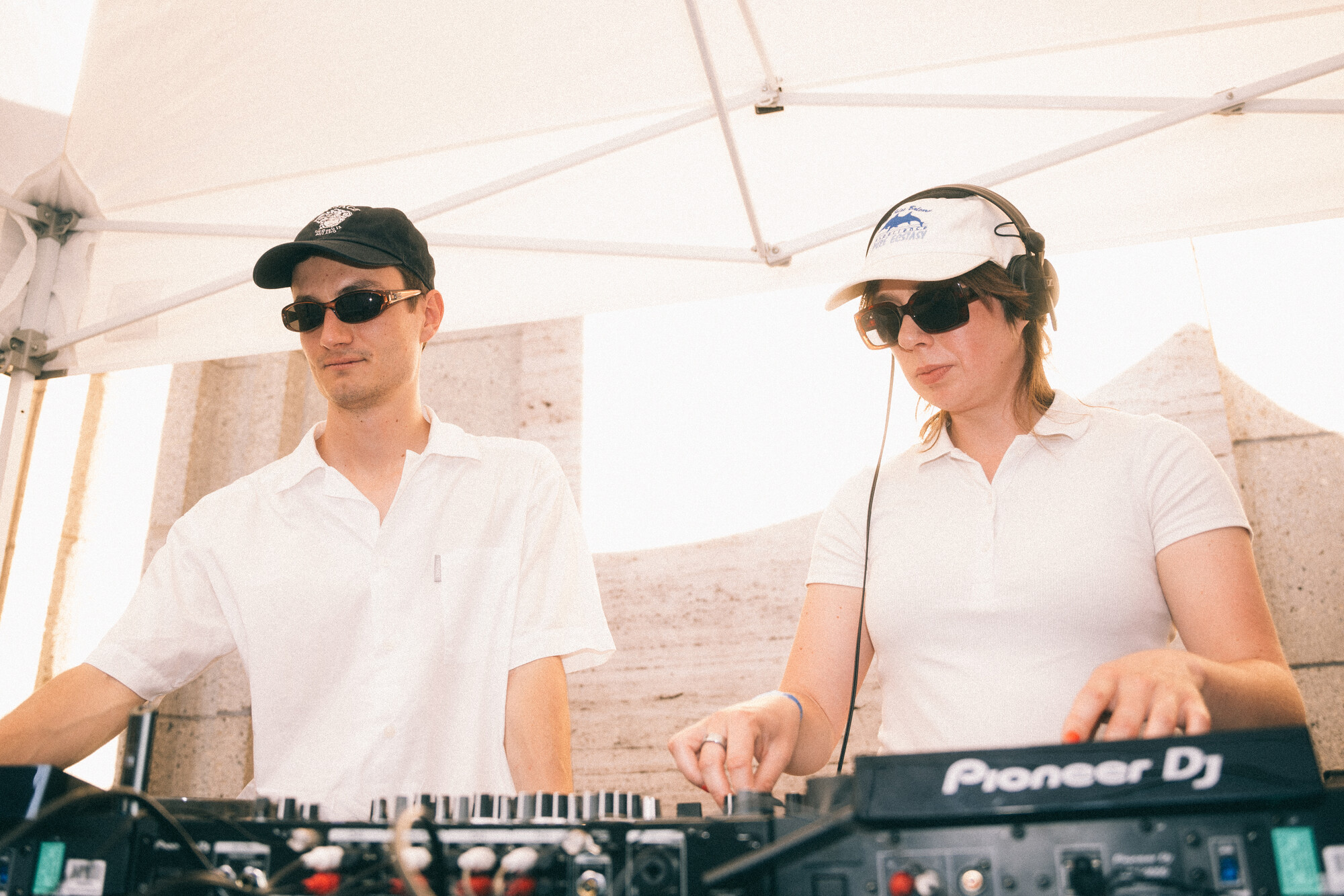Lena M und Summetotal legen mit Sonnenbrille und Kappe unter einem Sonnensegel an ihren DJ-Pulten auf.